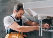male plumber in working overall fixing sink in bathroom