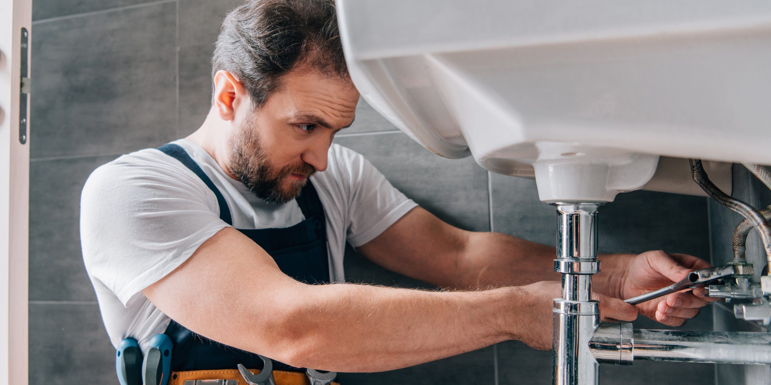 focused male plumber in working overall fixing sink in bathroom male plumber in working overall fixing sink in bathroom