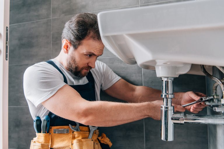 male plumber in working overall fixing sink in bathroom